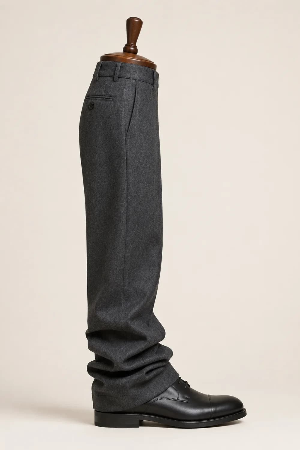 A charcoal trouser leg on a wooden display form over a black derby shoe, hanging with full break.