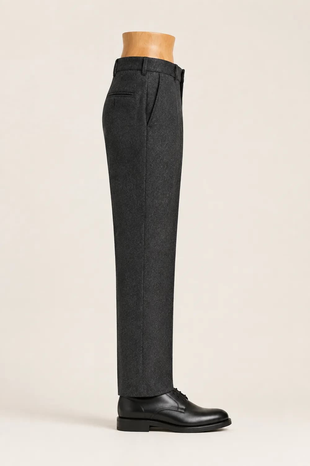 A charcoal trouser leg on a wooden display form over a black derby shoe, hanging with no break.