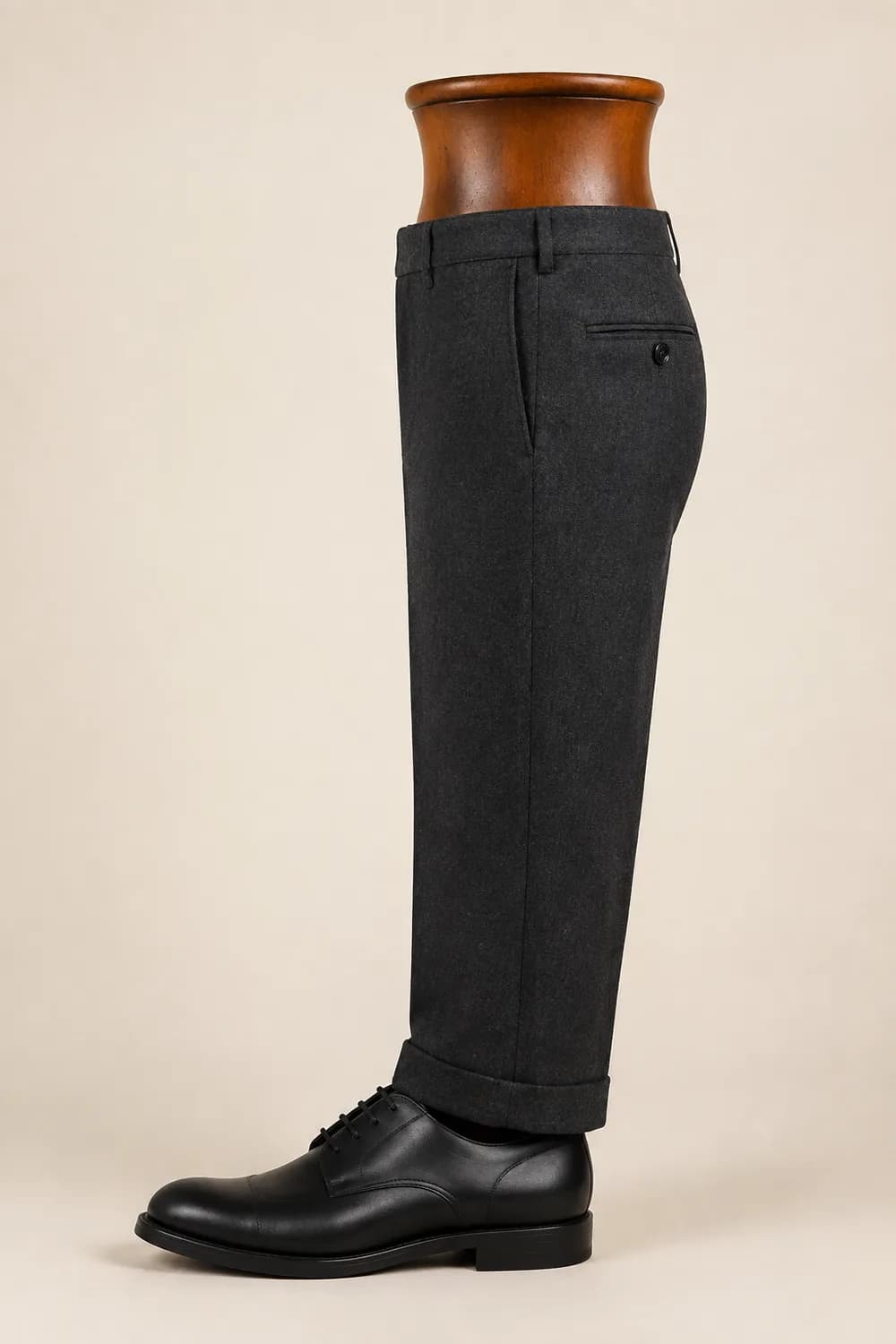 A charcoal trouser leg on a wooden display form over a black derby shoe, hanging with single break.