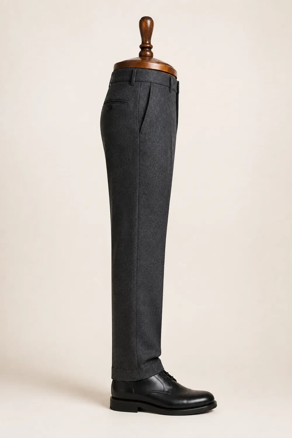 A charcoal trouser leg on a wooden display form over a black derby shoe, hanging with slight break.