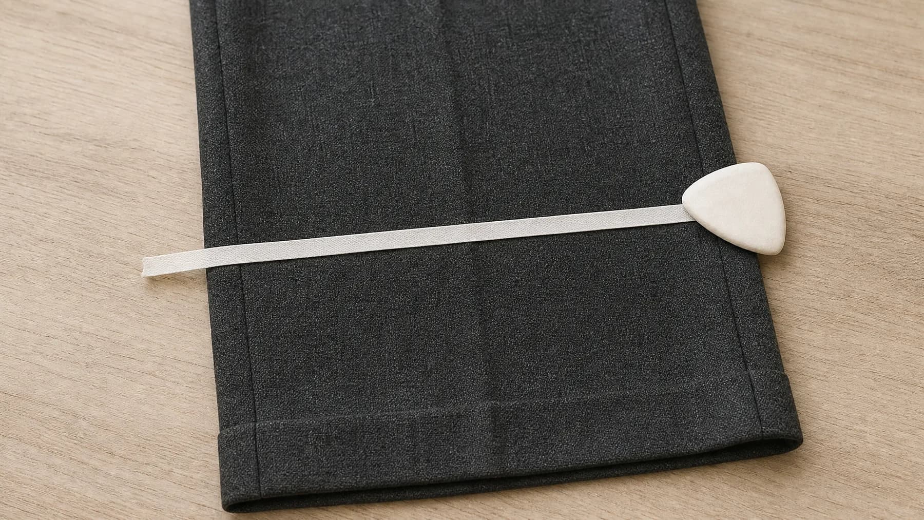A charcoal trouser leg laid flat with a tape laid across it marking a line, and a piece of tailor's chalk.